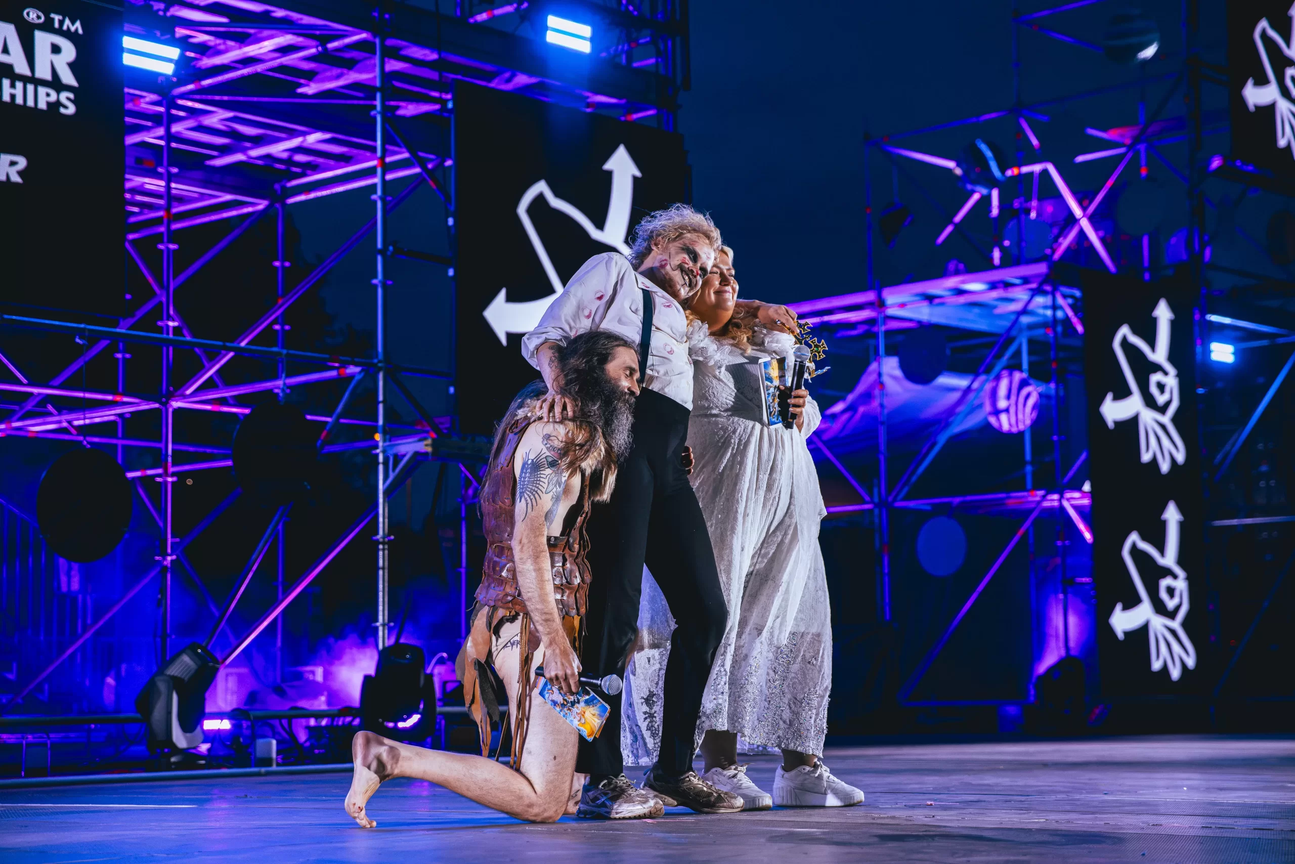 Aapo Rautio posa abrazado con dos participantes en el escenario de la final de guitarra de aire de Oulu.